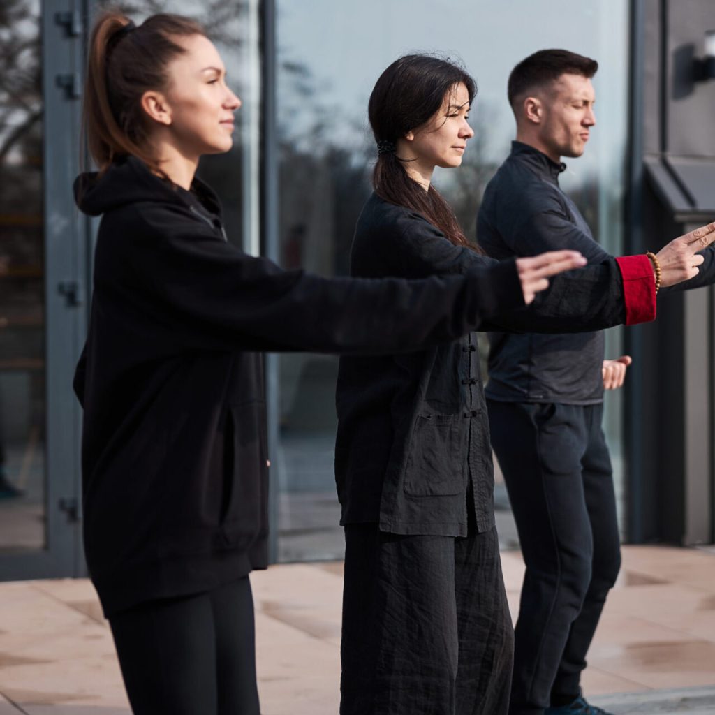 Wushu technique master staying between two pupils while making hand movement with two sticking fingers from left to right