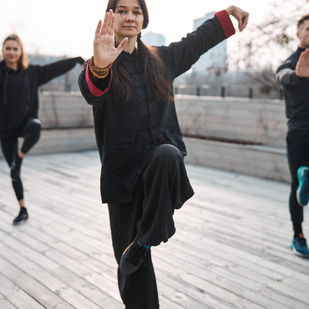 Focused female martial arts trainer teaching pair of students in background the way of keeping steady position on one leg
